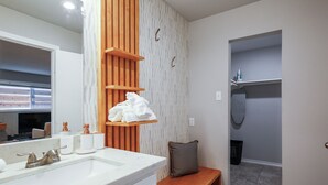 A bathroom with a white sink, wooden shelves, a bench, and a towel rack.