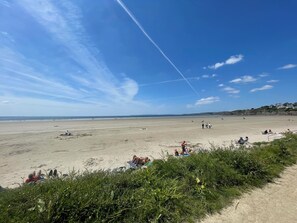 Una extensa playa de arena con gente tomando el sol y paseando.