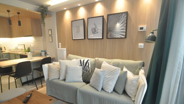 A modern living room with a sofa, a dining table, and chairs. There are framed pictures on the wall and a plant hanging above the table. - Zennova 71 Mondè Thessaloniki Apt (Thessaloniki)