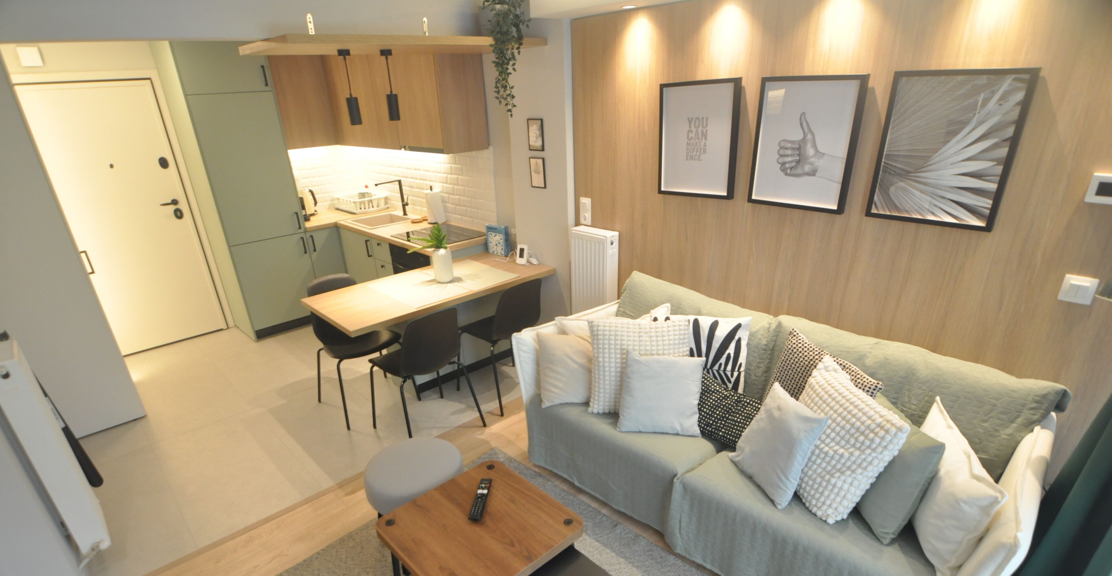 A compact living space with a kitchenette, a sofa with multiple cushions, a wooden coffee table, and a dining area with chairs.
