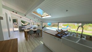 A modern kitchen with a large island, a dining area with a table and chairs, and a view of the outdoors. - Villa 71 Hossegor with heated pool, basketball, pétanque and vacation atmosphere (Soorts-Hossegor)