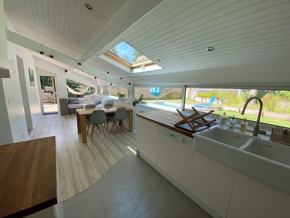 A modern kitchen with a large island, a dining area with a table and chairs, and a view of the outdoors.