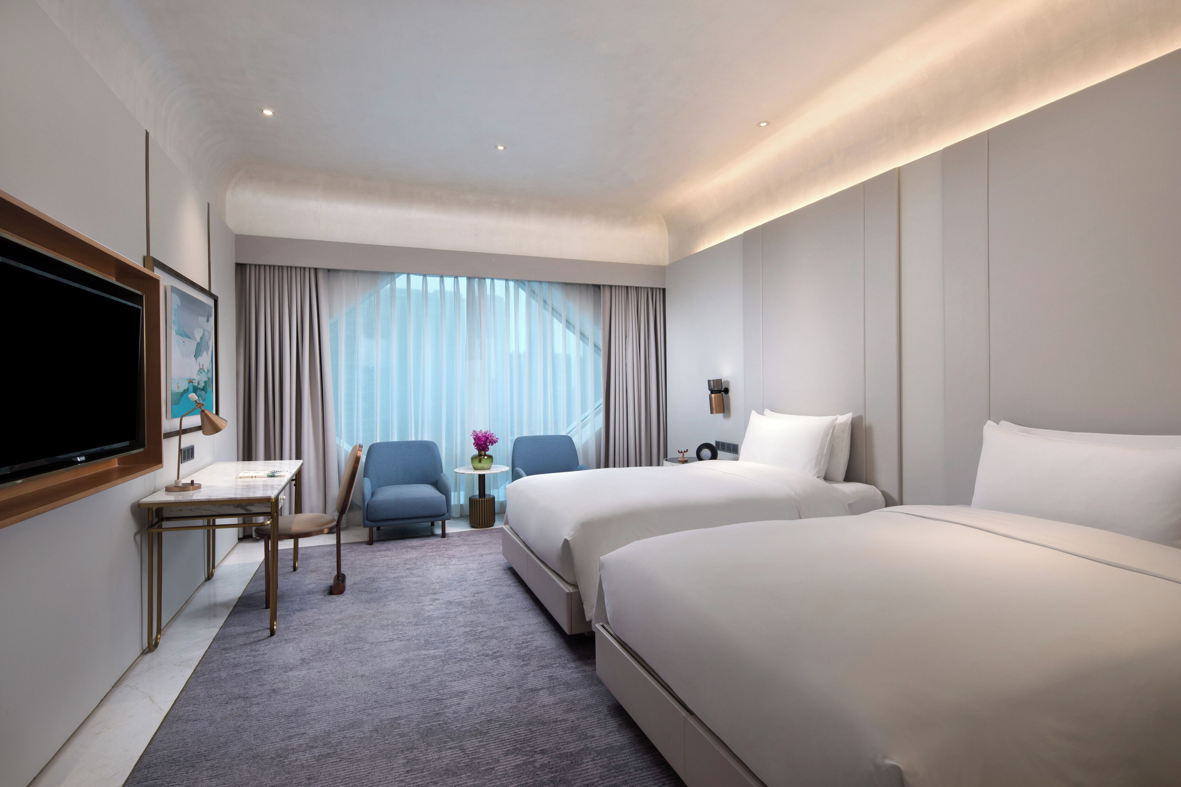 Een hotelkamer met een groot bed, een kleiner bed, een bureau met stoel, een televisie en een raam met gordijnen.