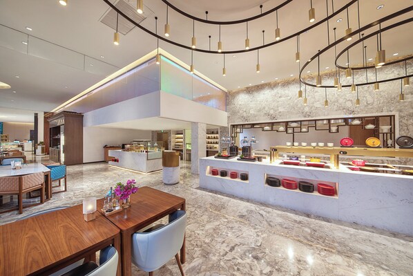 A modern hotel lobby with a marble floor, a wooden reception desk, and a seating area with tables and chairs.