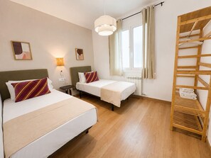 Habitación de hotel con dos camas, un armario de madera, una mesita de noche con lámpara y una ventana con cortinas.