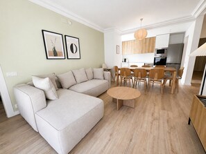 A modern living room with a sectional sofa, a round coffee table, and a dining area with wooden chairs and a table. - Stay U-nique Apartments Balmes II (Barcelona)