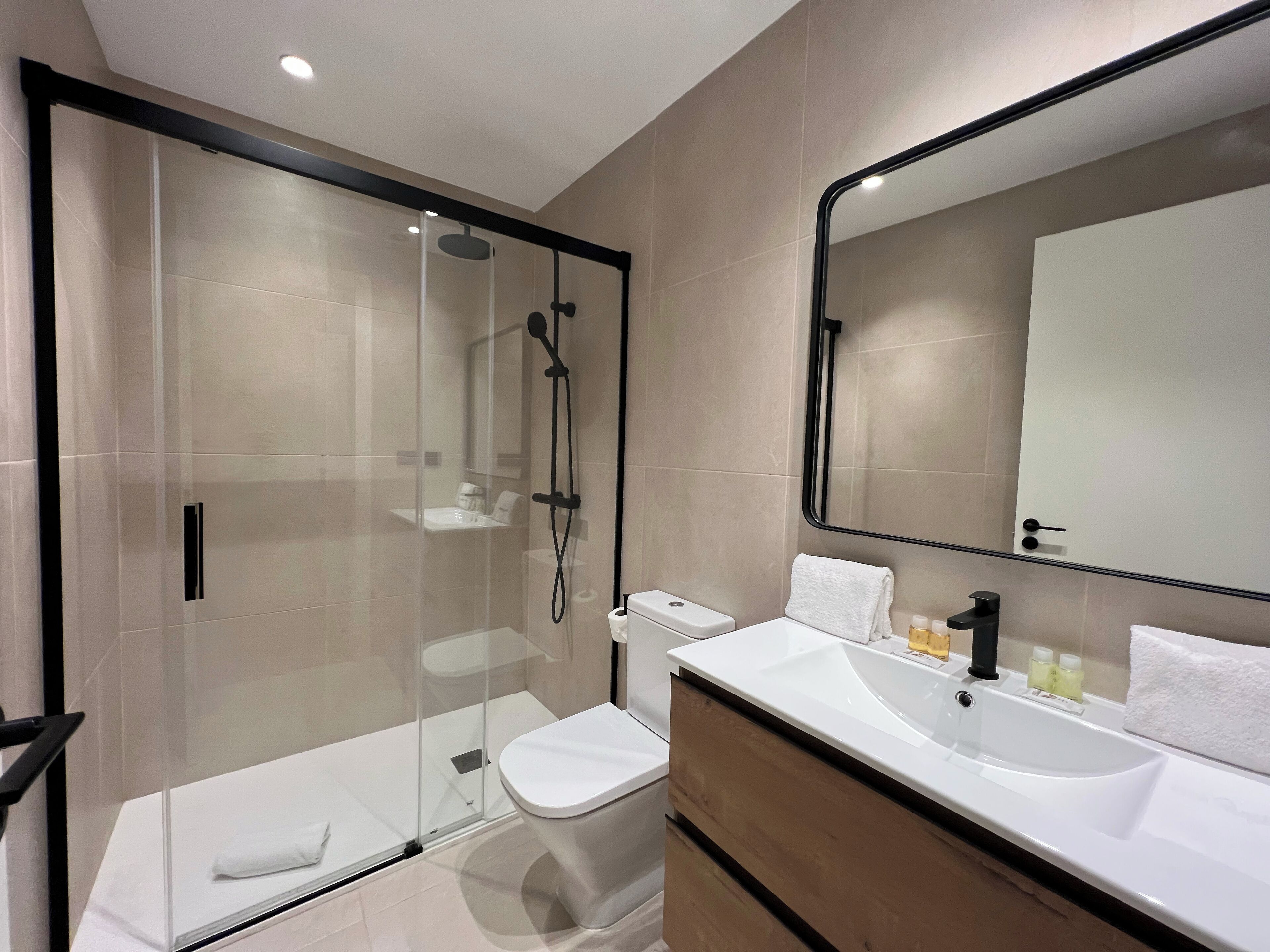 Une salle de bain moderne avec une douche à parois de verre, des toilettes blanches, un lavabo avec un miroir et une serviette accrochée au mur.