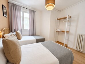 A bedroom with two beds, a window with curtains, a radiator, and a wooden shelf with folded towels. - Stay U-nique Apartments Balmes II (Barcelona)