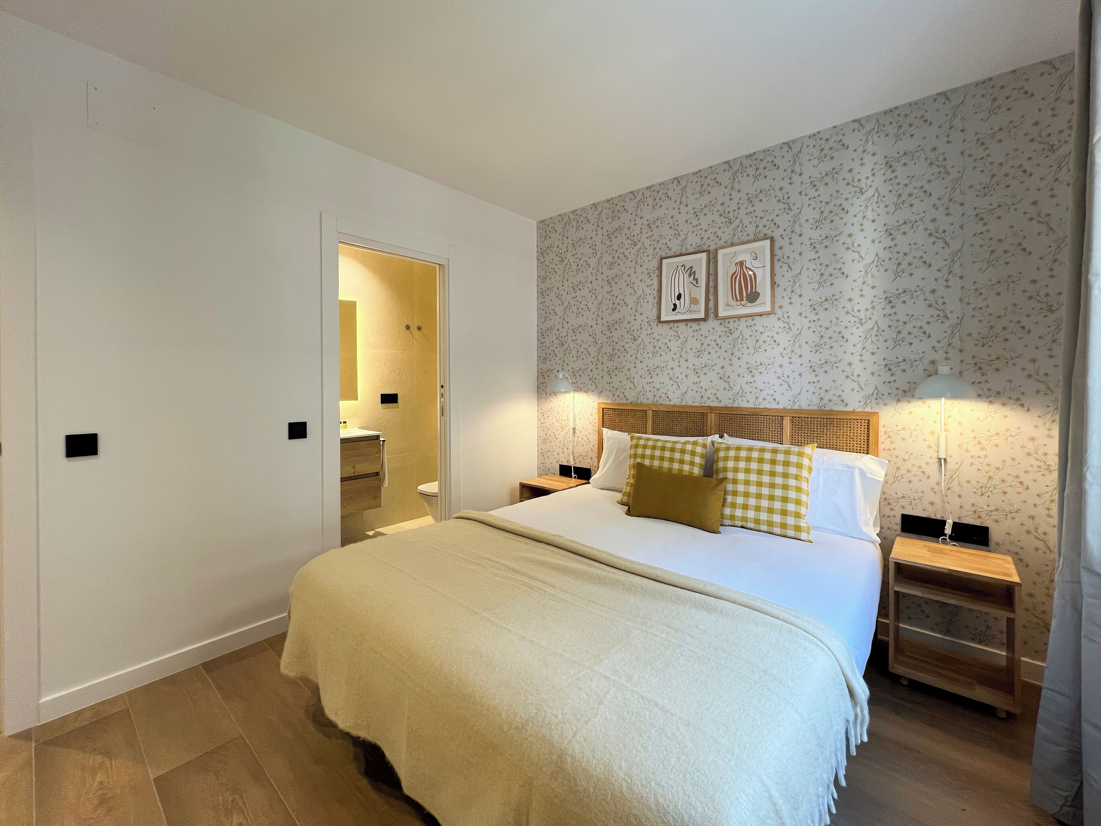 Een slaapkamer met een bed, nachtkastjes, een spiegel en een deur naar een badkamer.