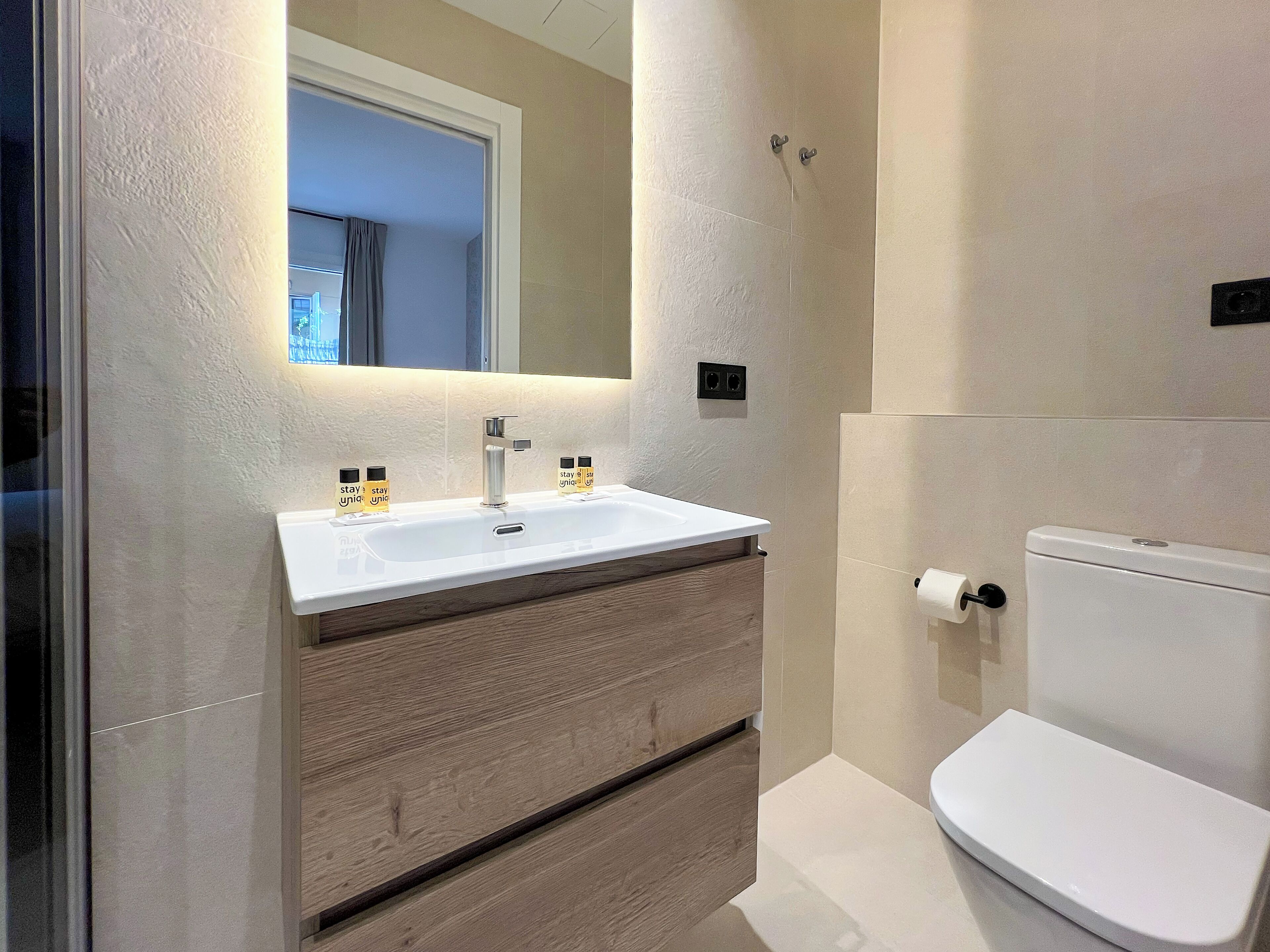 Een badkamer met een wit wastafel, een spiegel, een toilet en houten kastjes.