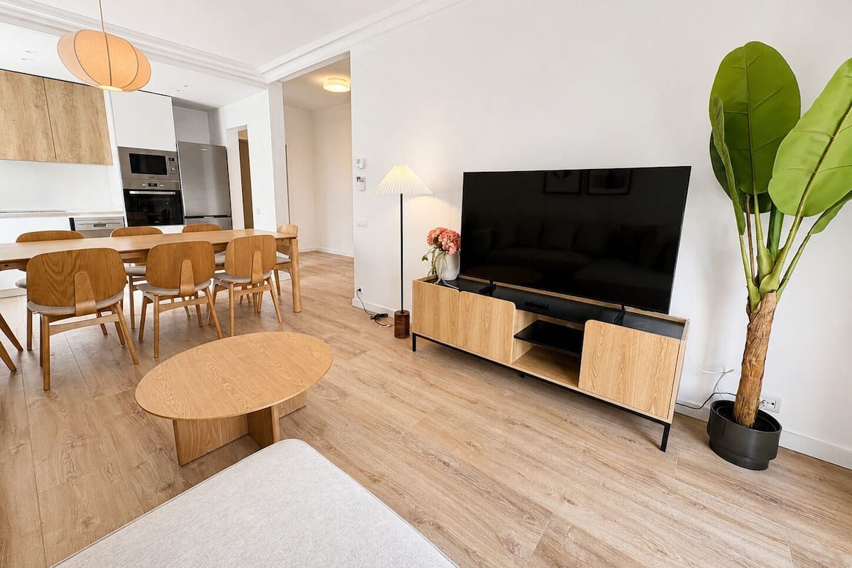 Ein modernes Wohnzimmer mit Fernseher, Holzmöbeln, einem Essbereich und einer Topfpflanze.