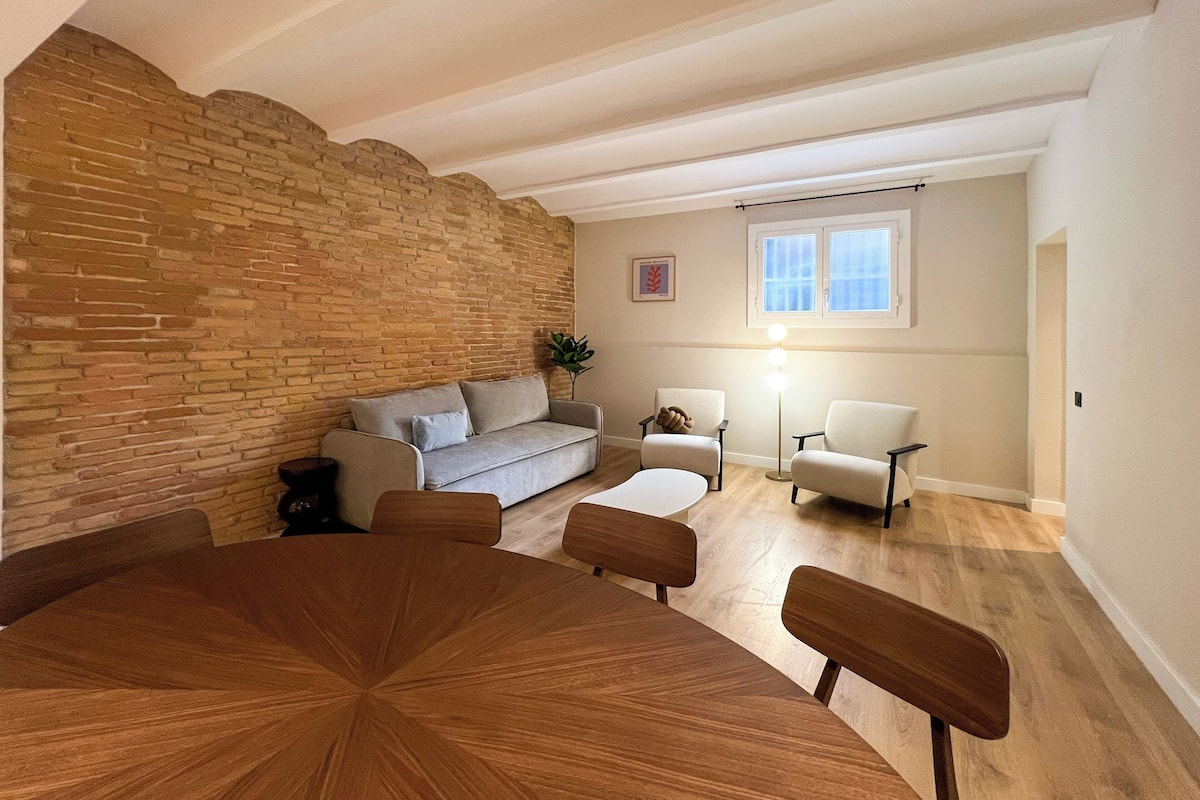 Ein modernes Wohnzimmer mit Backsteinwand, einer Couch, zwei Sesseln, einem Couchtisch und einer Stehlampe.