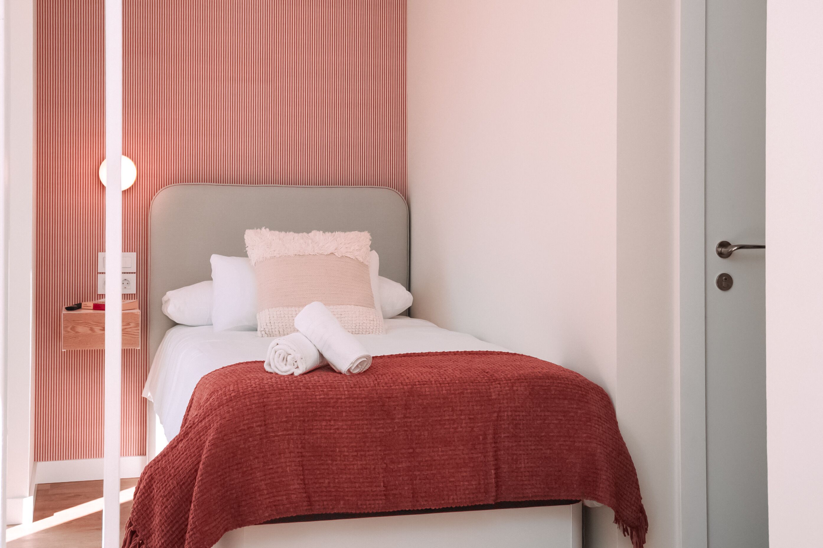 Un lit bien fait, avec une couverture rouge, des oreillers blancs et une tête de lit blanche.