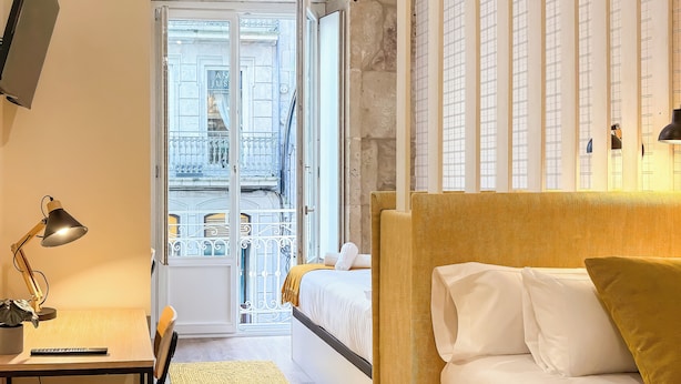 Una habitación de hotel moderna con una cama, un escritorio y vistas a un paisaje urbano a través de un ventanal grande.