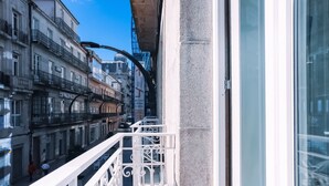 Una calle estrecha flanqueada por edificios, barandilla de balcón blanca y cielo azul despejado.