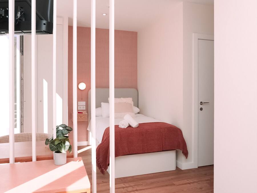 Un dormitorio con cama, mesita de noche, planta en maceta y una puerta.