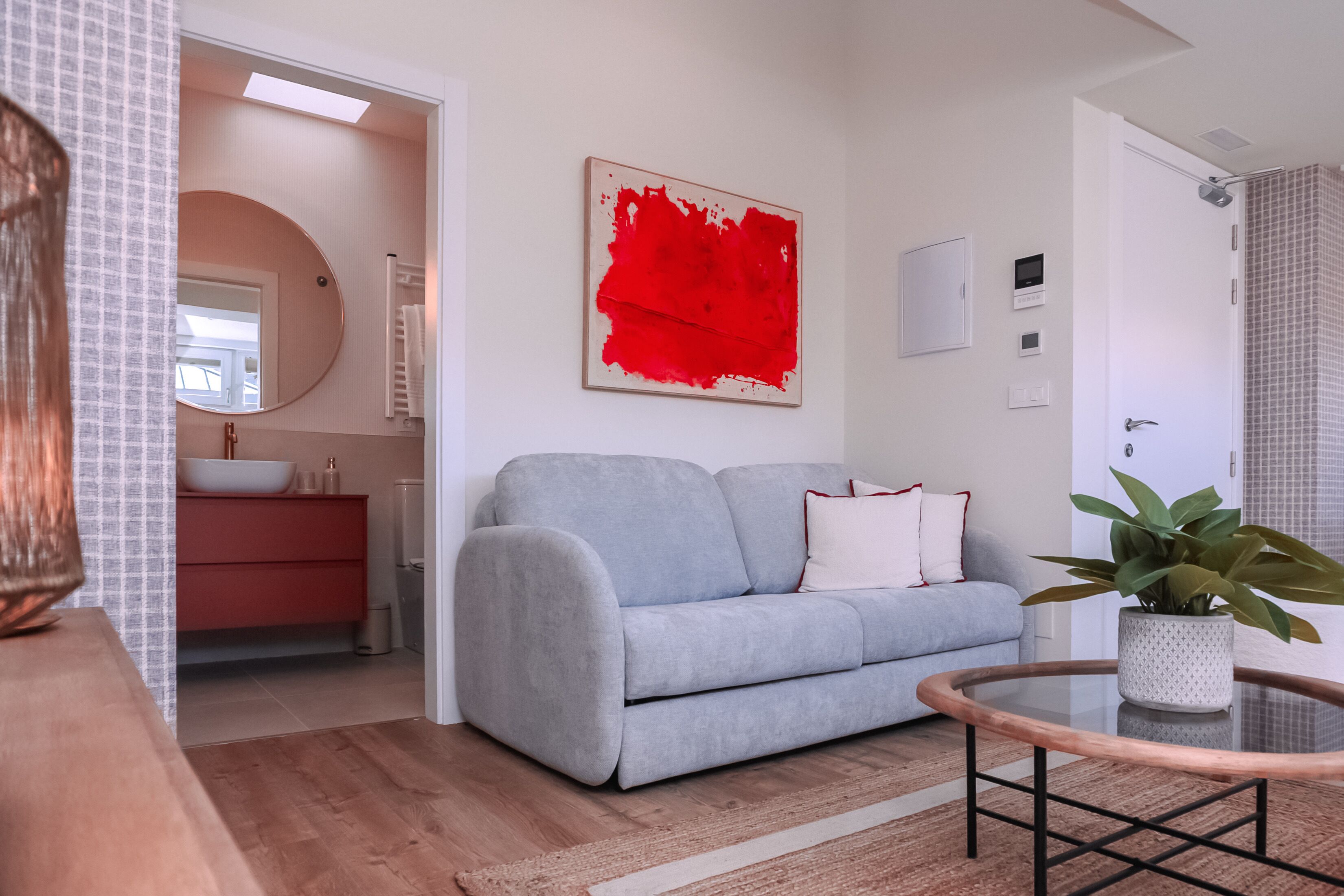 A modern living room with a grey sofa, a round coffee table, and a red abstract painting on the wall.