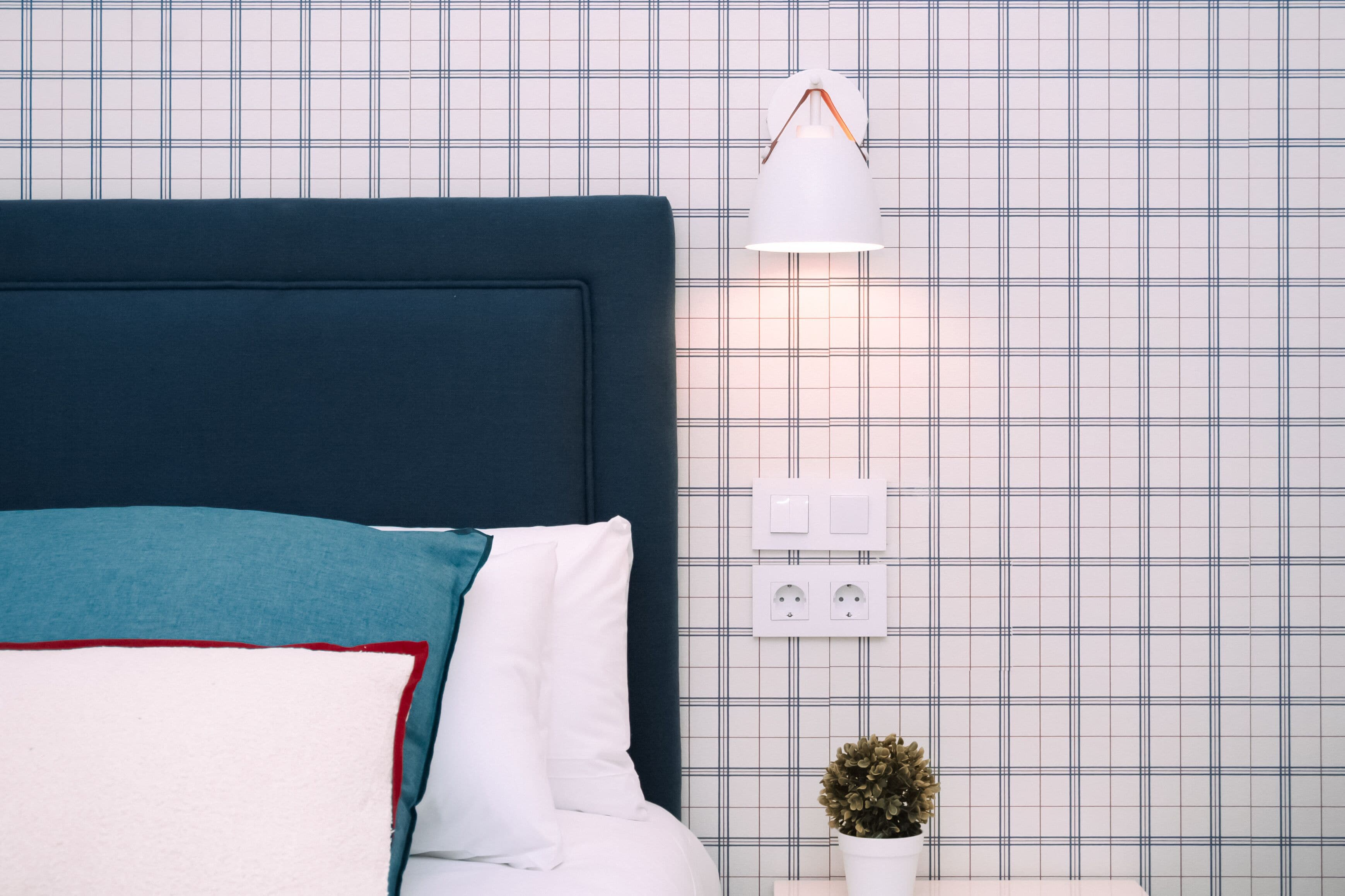 A neatly made bed with a dark headboard, white and teal pillows, and a small potted plant on the nightstand.