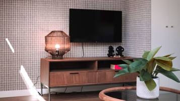 Een moderne woonkamer met een houten tv-meubel, een flatscreen televisie, een lamp en een potplant.