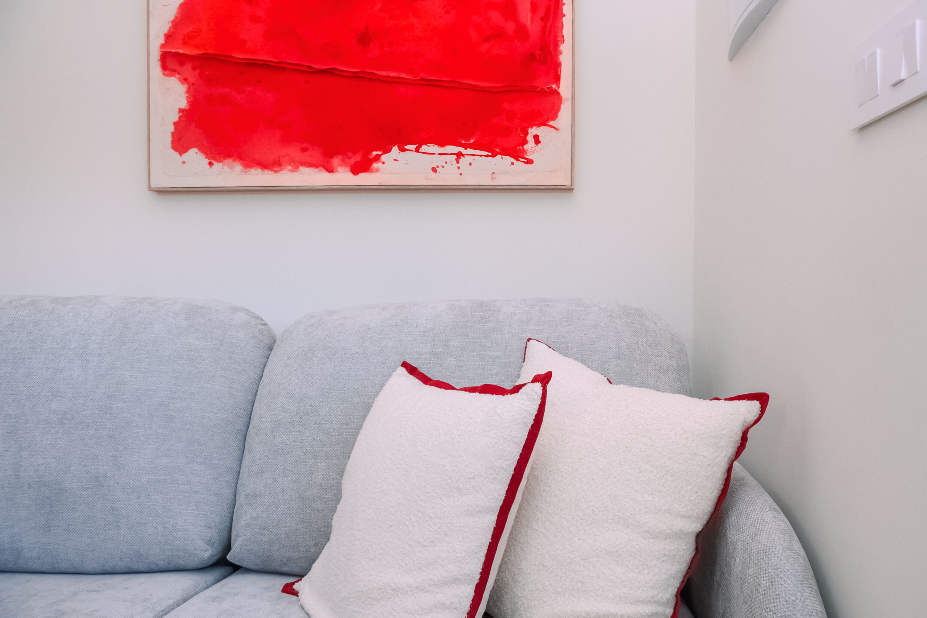 A grey sofa with a white cushion and a red accent cushion.