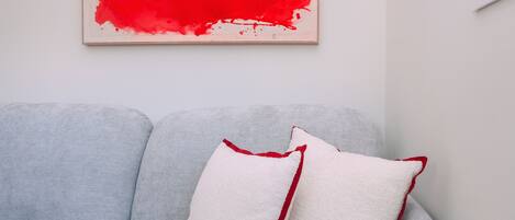 A grey sofa with a white cushion and a red accent cushion.