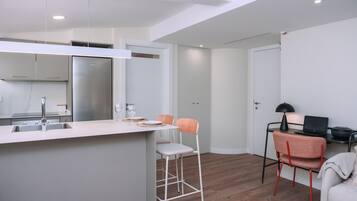 Una cocina moderna con encimera blanca, electrodomésticos de acero inoxidable y dos taburetes de bar.