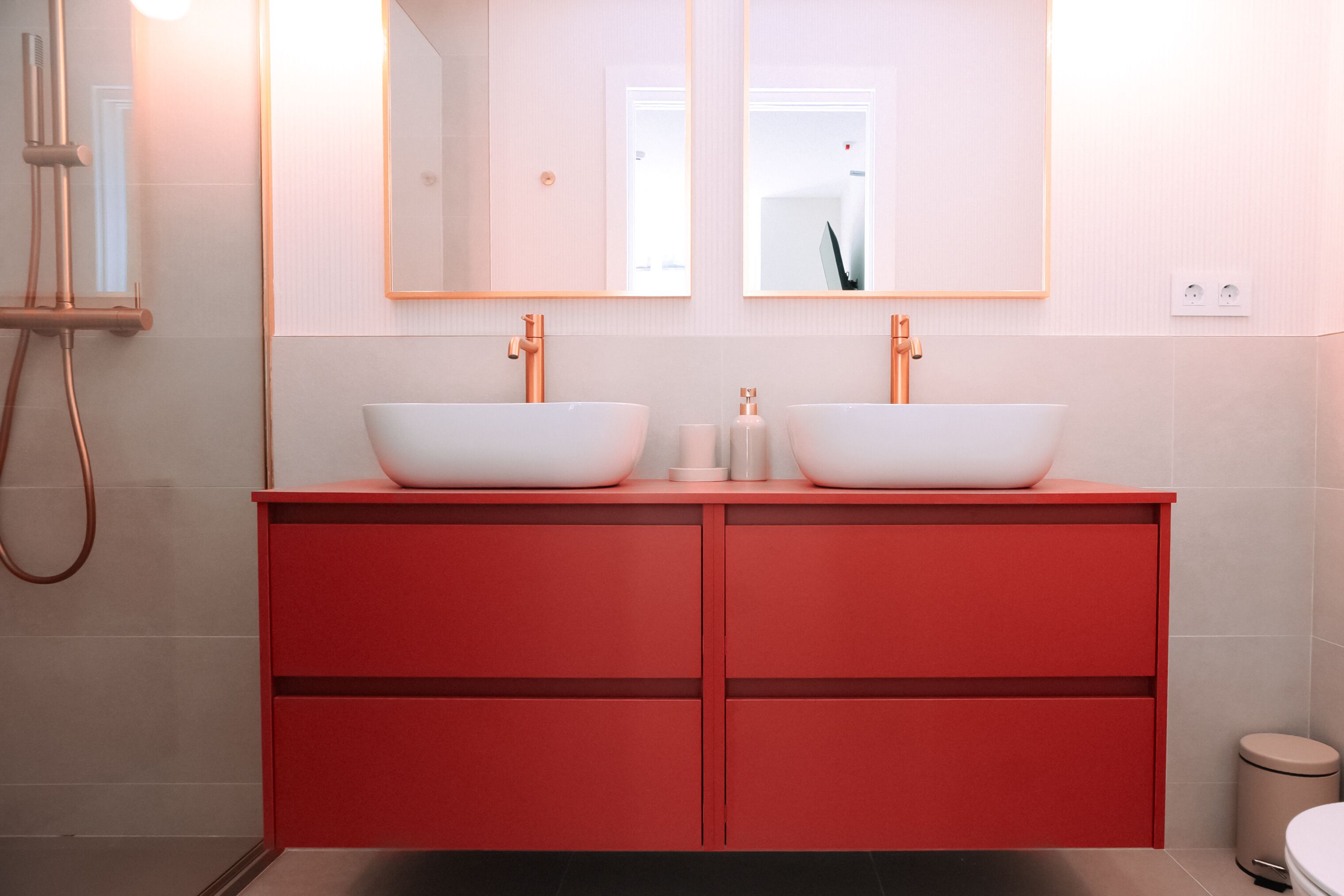 Ein modernes Badezimmer mit einem roten Waschtisch, zwei weißen Waschbecken und einem großen Spiegel darüber.