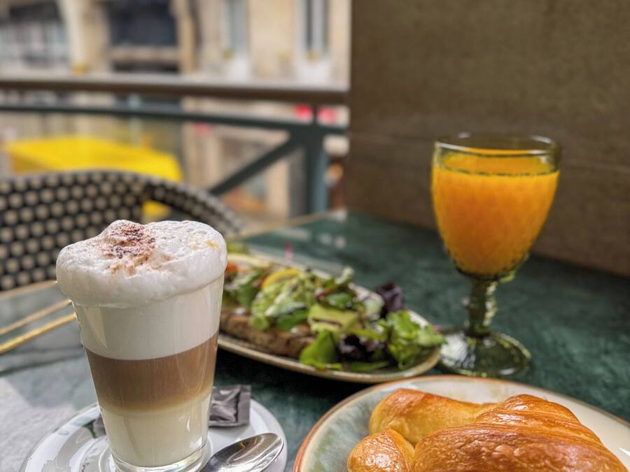 Una mesa con una bebida, un plato de comida y un vaso de jugo en un balcón con vista a edificios.