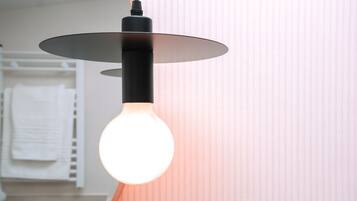 A modern light fixture with a spherical bulb, mounted on a black base, in a room with a striped wall and a white towel hanging on a rack.