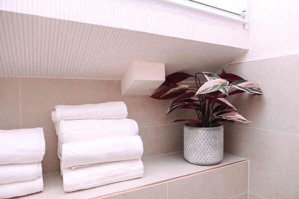 A bathroom with stacked white towels, a potted plant, and a white shelf.