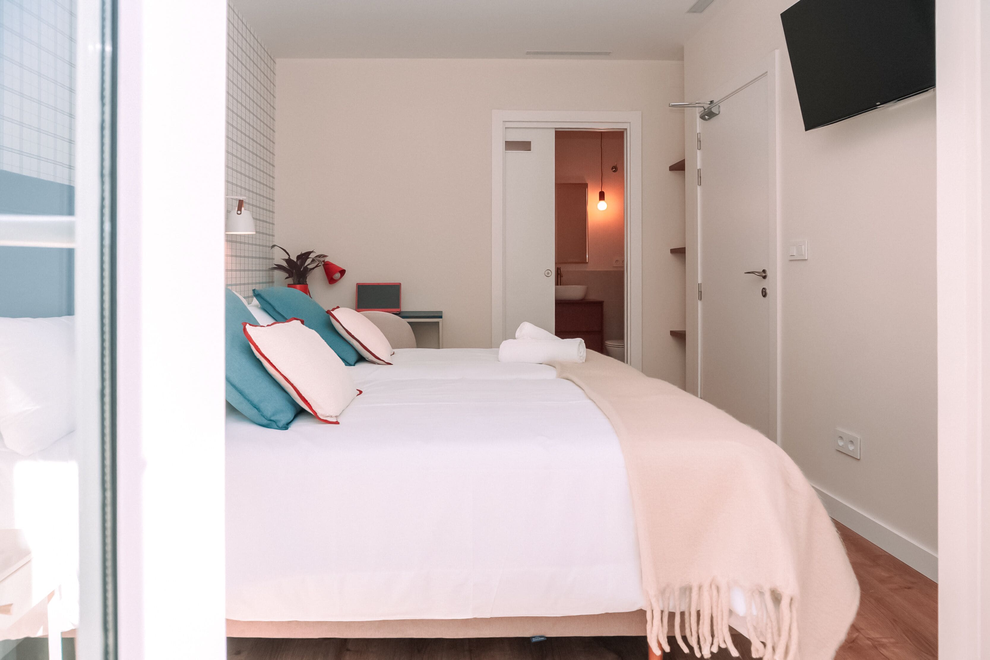 Une chambre à coucher avec un lit, un téléviseur fixé au mur et une porte donnant sur une salle de bain.