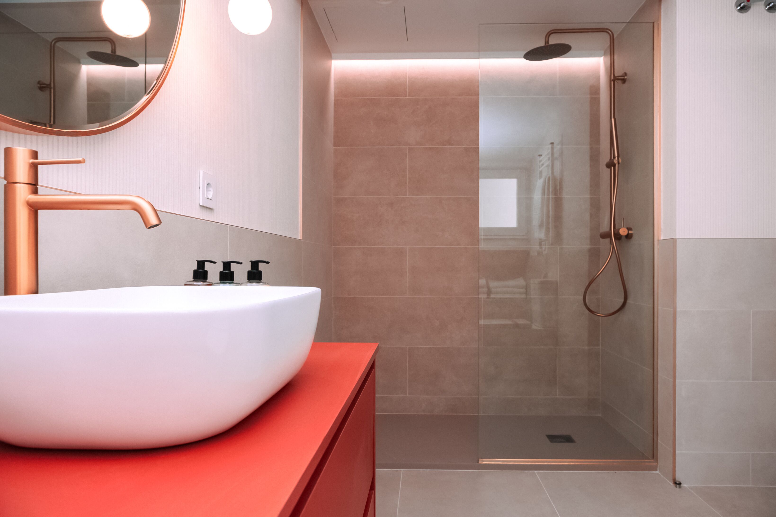 Un baño moderno con lavamanos blanco, accesorios de cobre y ducha con cerramiento de vidrio.