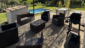 Un patio exterior con mobiliario de mimbre, una piscina y una parrilla.