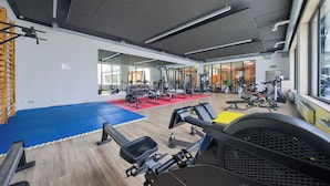 Ein Fitnessraum mit Trainingsgeräten, einem blauen Mattenbereich und einem Fenster mit Außenblick.