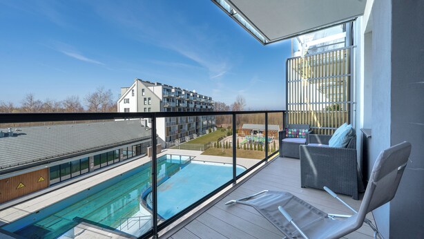Ein Balkon mit Blick auf ein Schwimmbecken, Gartenmöbel und ein Gebäude im Hintergrund.