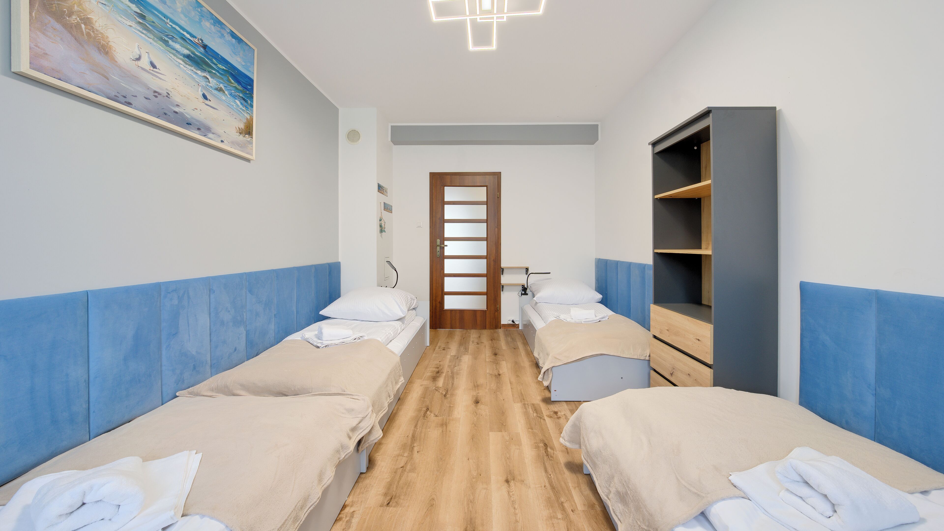 A hotel room with two beds, a wooden floor, a wardrobe, and a painting on the wall.
