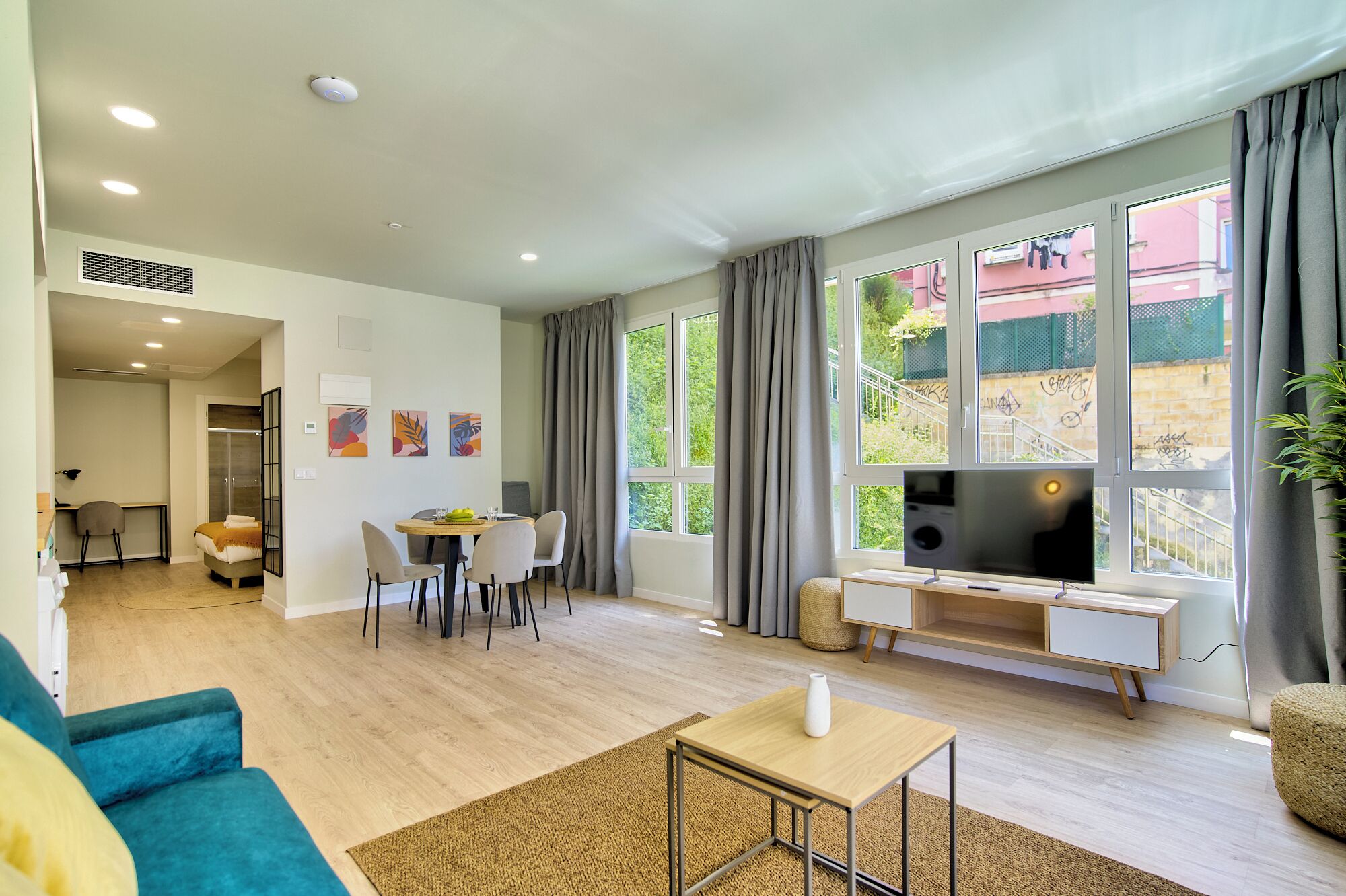 A modern living room with a dining area, large windows, and a TV.