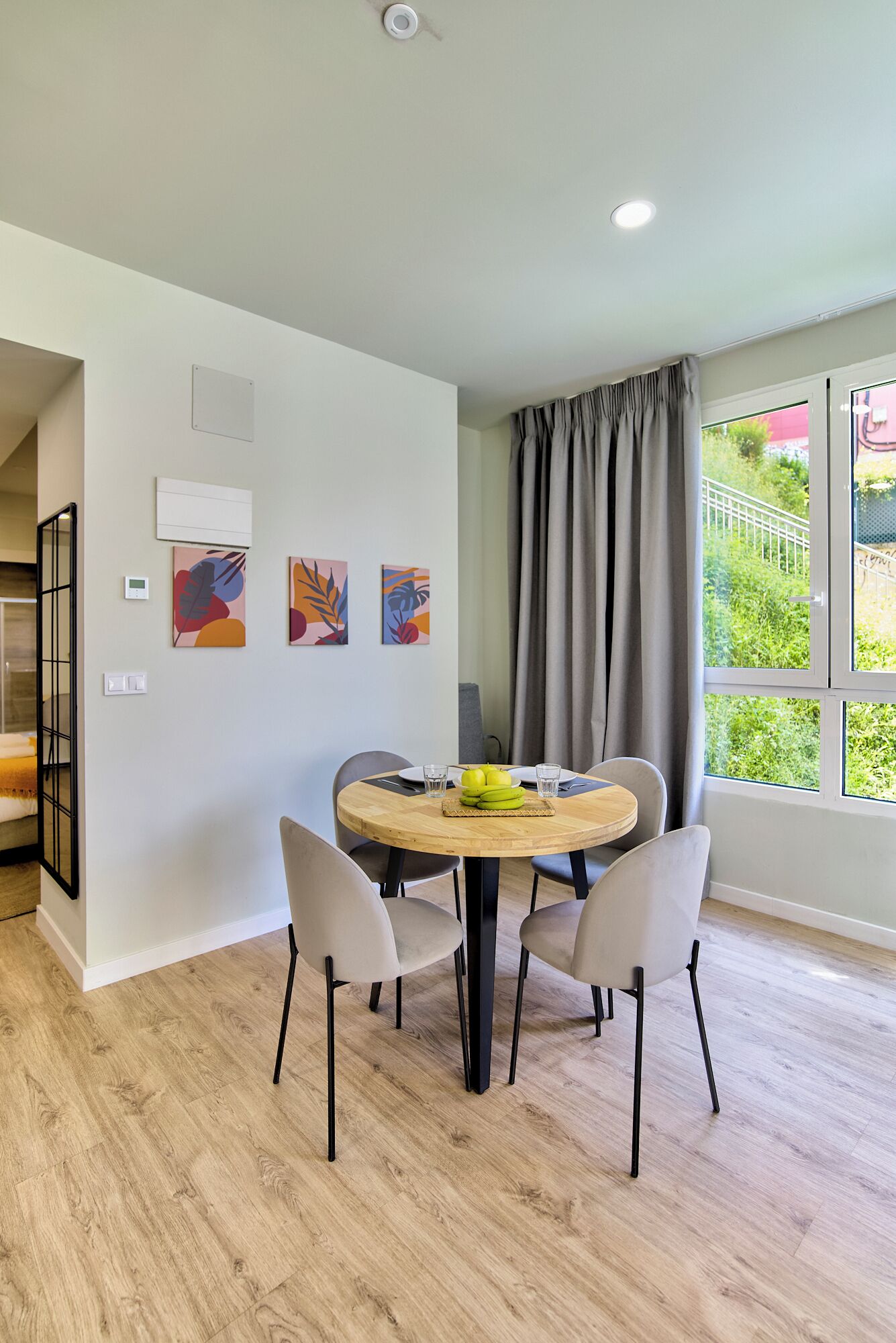 A modern dining area with a round wooden table, four chairs, and a small fruit display.