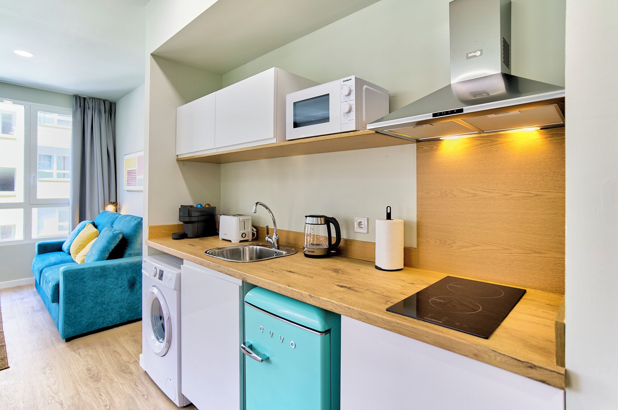 A compact kitchenette with a microwave, toaster, kettle, and a small dishwasher.