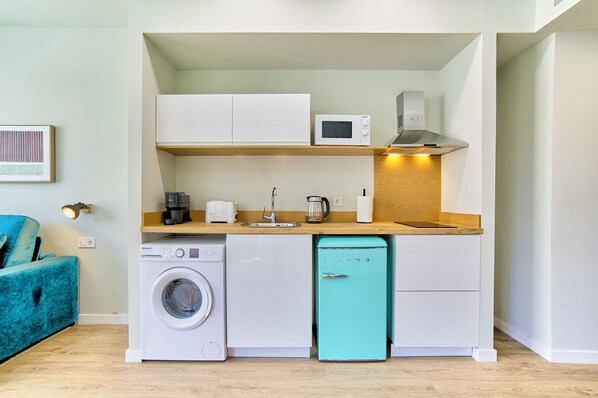 Una kitchenette compacta con lavadora, lavavajillas y un refrigerador compacto color verde azulado.