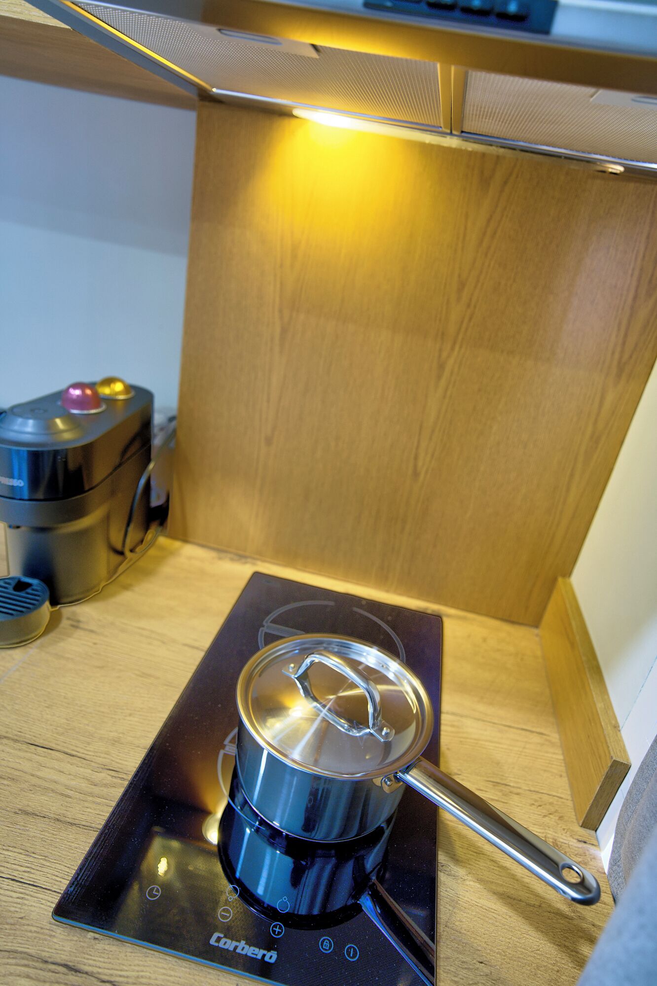 A compact cooking setup with a portable stove and pot, located in a small kitchen area with wooden cabinetry.