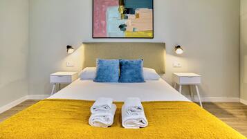 Une chambre d’hôtel avec un lit, deux tables de chevet, une tête de lit, un tableau et deux lampes.
