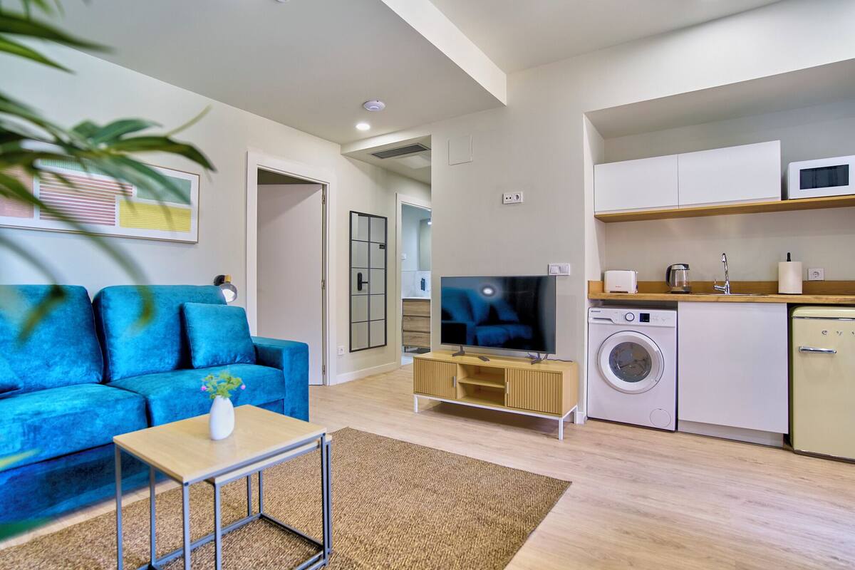 Un appartement moderne avec un canapé bleu, un t éléviseur, un lave-linge et une kitchenette.