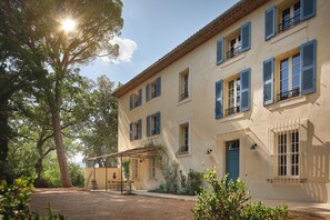 Un bâtiment à deux étages, doté d’une façade beige, de volets bleus et d’un patio abrité.