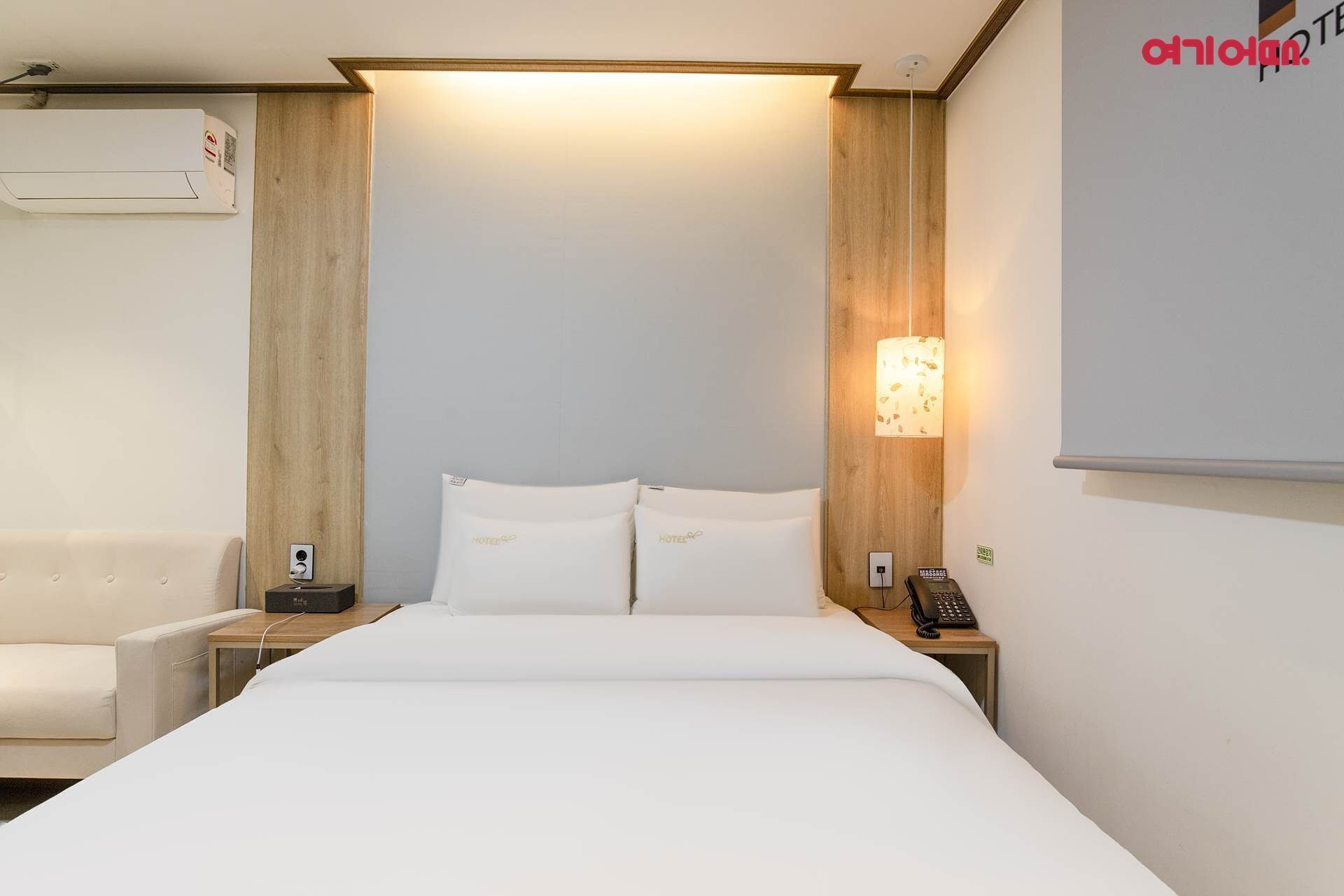 A hotel room with a bed, bedside tables, a lamp, and a wall-mounted air conditioner.