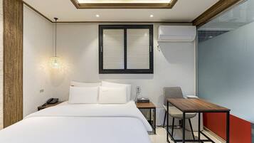 Une chambre d’hôtel comprenant un lit, une table de chevet, une lampe, une fenêtre, un appareil de climatisation et un bureau avec une chaise.