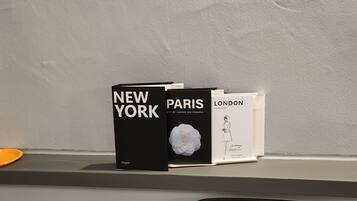 A shelf with books titled 'New York,' 'Paris,' and 'London,' and a white plate with a flower.