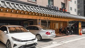 A hotel entrance with a traditional tiled roof, a signboard, and parked cars and motorcycles. - MARU HOTEL (Seoul)