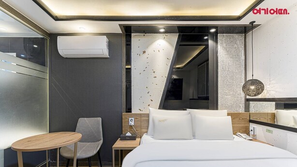 A modern hotel room with a bed, bedside table, chair, and an air conditioning unit. - MARU HOTEL (Seoul)