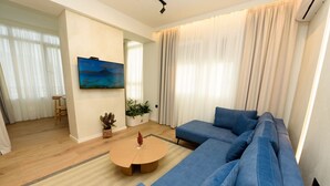 A modern living room with a blue sofa, a round coffee table, and a painting on the wall. - E&K Apartment 02 , Sea view, Free Parking (Vlora)